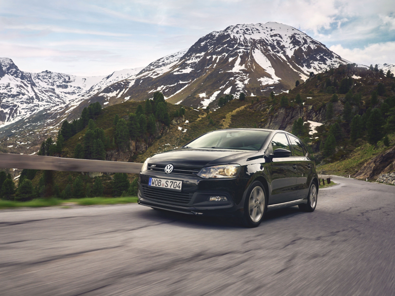 VW Polo fährt Straße entlang, im Hintergrund Berge, die leicht mit Schnee bedeckt sind
