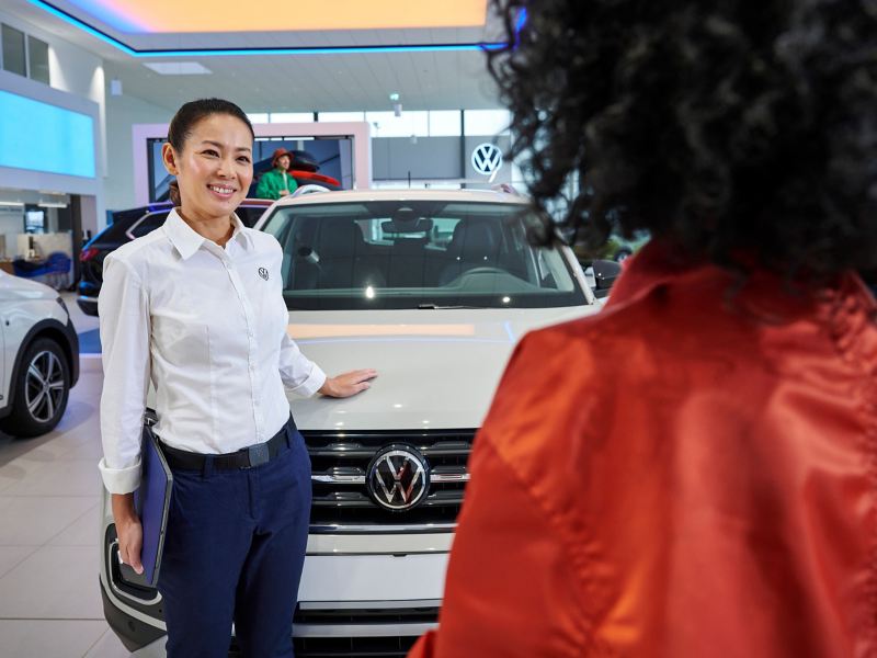 Eine VW Servicemitarbeiterin und eine Kundin im Autohaus vor einem VW Neuwagen