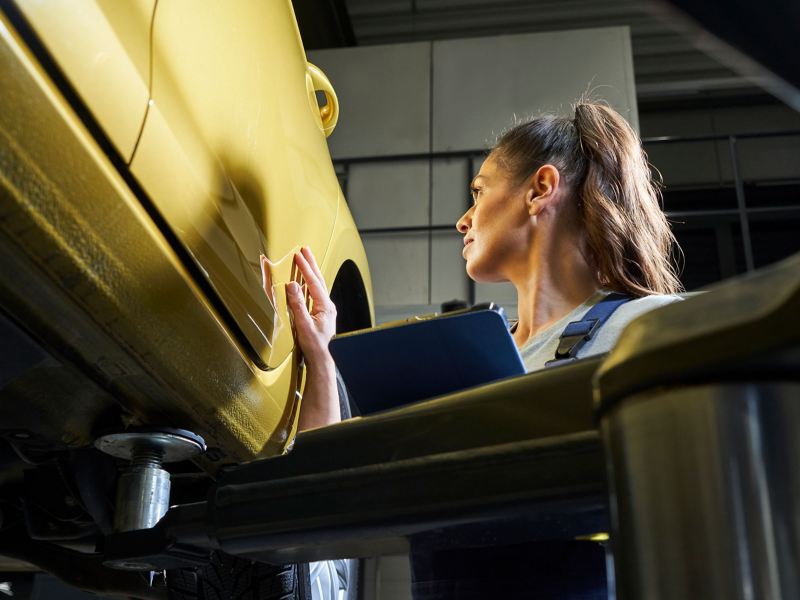 VW service employee with clipboard looks at the paintwork of a VW car