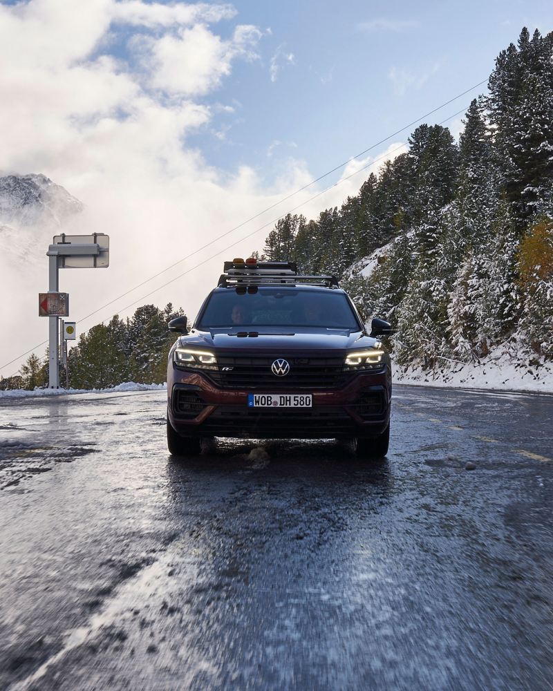 A Touareg on a wet road with thawed snow, snowy mountains in the background