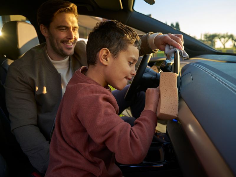 Father and son clean interior of VW vehicle with cloth and sponge