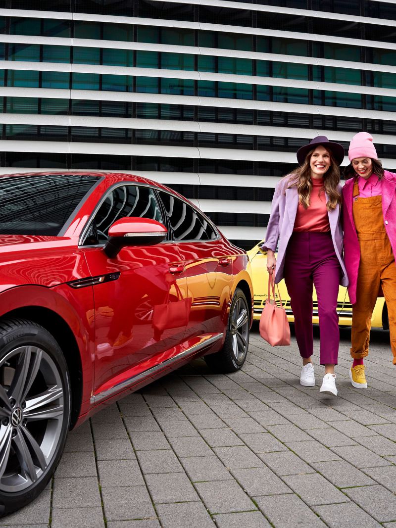 Zwei Frauen mit Einkaufstaschen neben ihren beiden Volkswagen – VW Aktionen und Angebote
