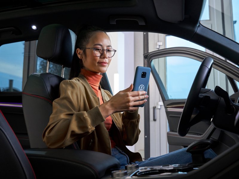Kobieta sprawdzająca telefon w samochodzie VW – pomoc dotycząca aplikacji i usług cyfrowych
