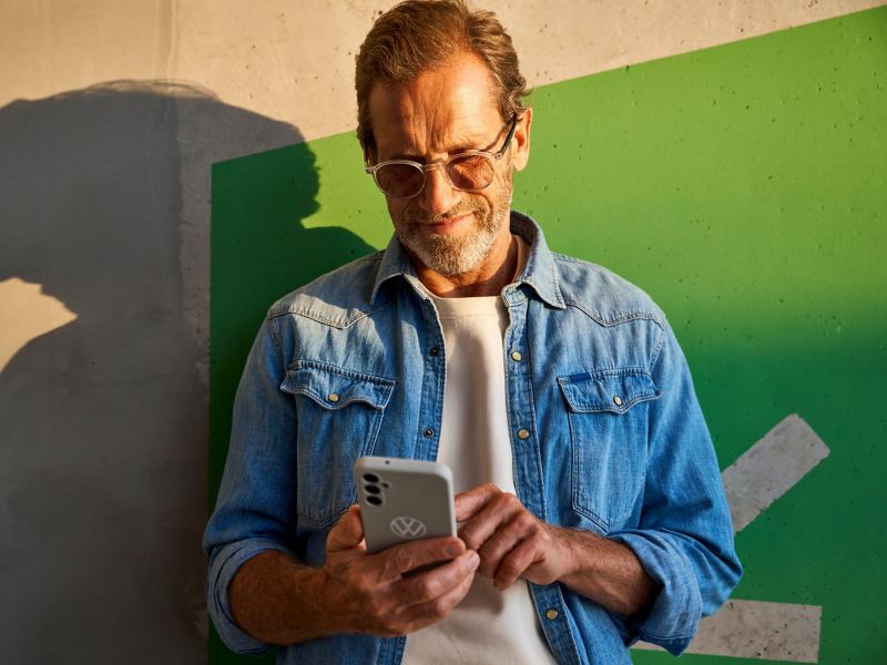 Man leaning against a wall and books Driving Experience appointment on his smartphone