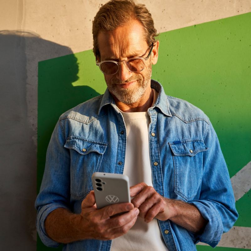 Man leaning against a wall and books Driving Experience appointment on his smartphone