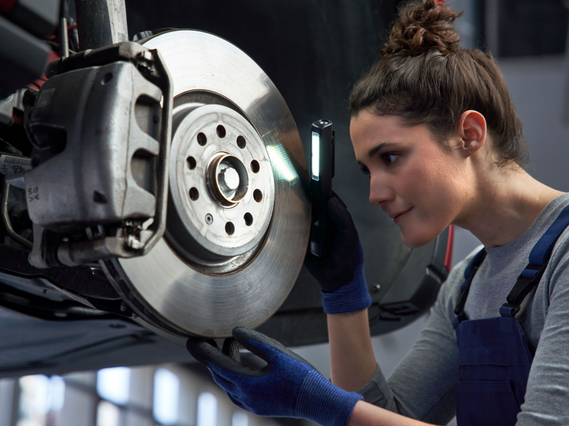 Une employée du service entretien VW inspecte les freins d’une voiture VW à l’aide d’une lampe