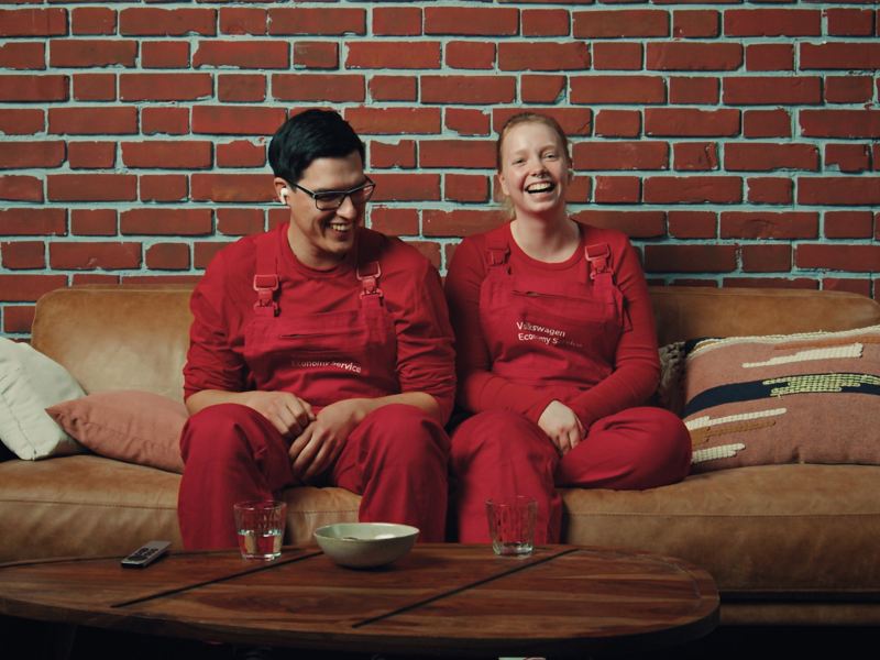 Zwei Mitarbeiter des Volkswagen Economy Service  sitzen auf einer Couch, lachen und reagieren gemeinsam auf ein Video