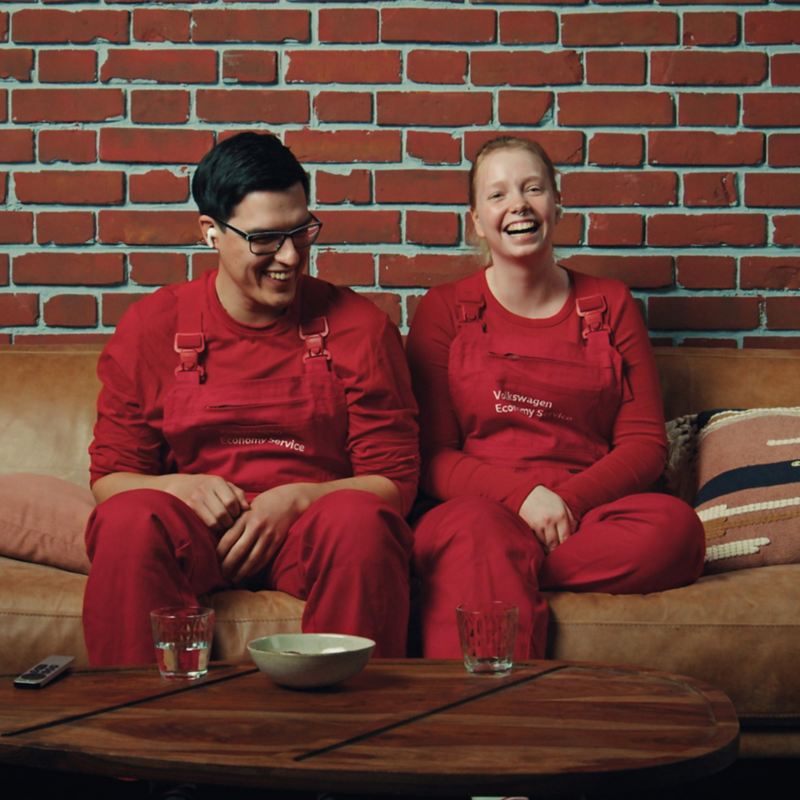 Zwei Mitarbeiter des Volkswagen Economy Service  sitzen auf einer Couch, lachen und reagieren gemeinsam auf ein Video