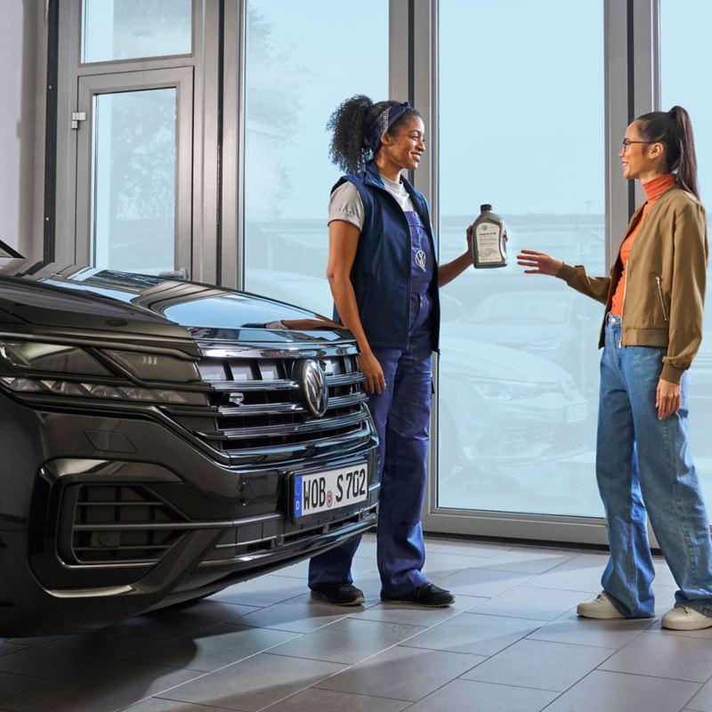 VW service employee hands customer a bottle of engine oil next to a VW Touareg