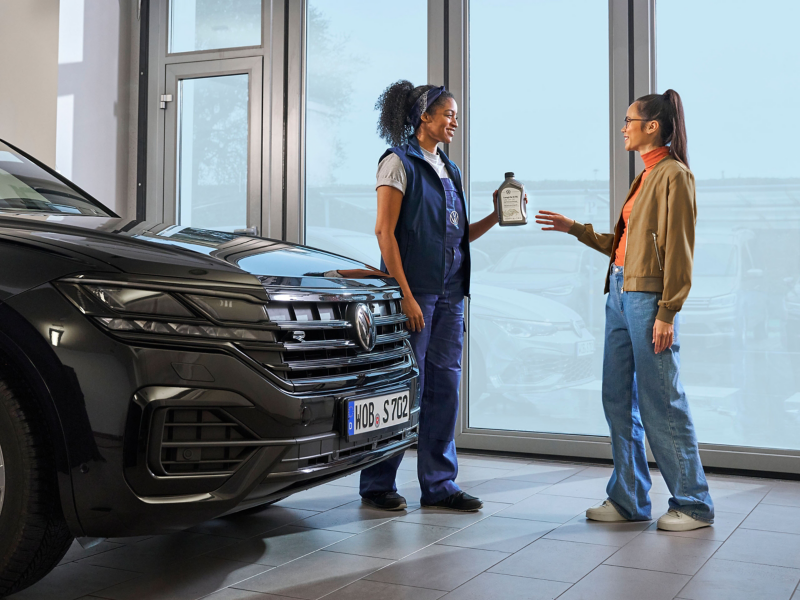 VW service employee hands customer a bottle of engine oil next to a VW Touareg