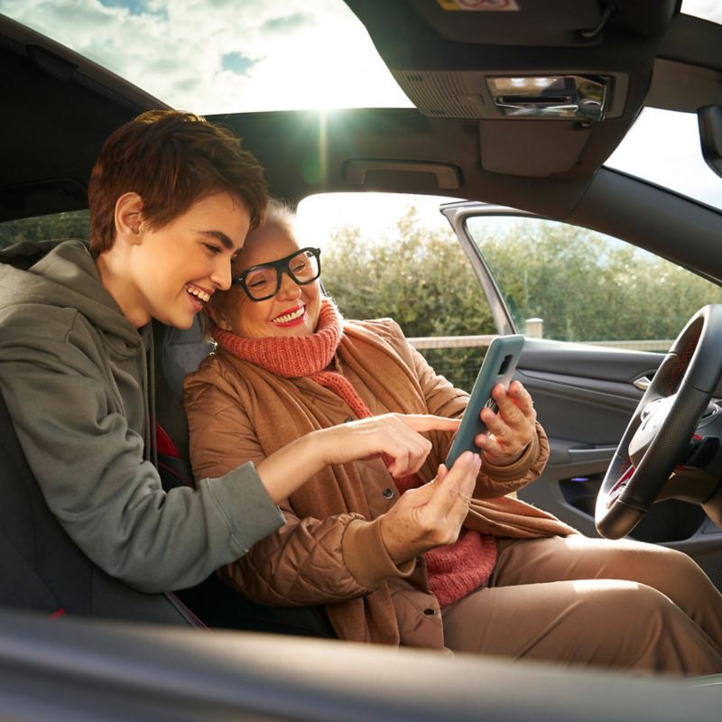 Two women in a VW with open driver door looking at smartphone – Entertainment and electronics