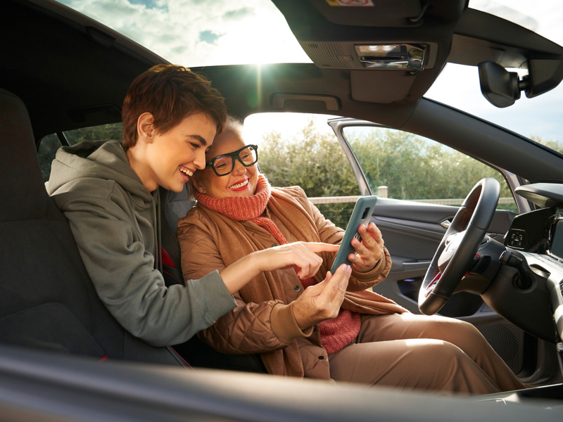 Two women in a VW with open driver door looking at smartphone – Entertainment and electronics