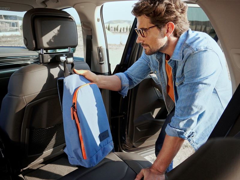 Man hangs backpack on a VW Accessories bag hook attached to the back seat of a VW car