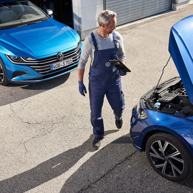 Un mecánico de Volkswagen junto a dos coches azules, uno con el capó abierto