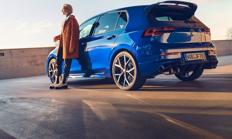 A woman leans against her blue VW Golf R