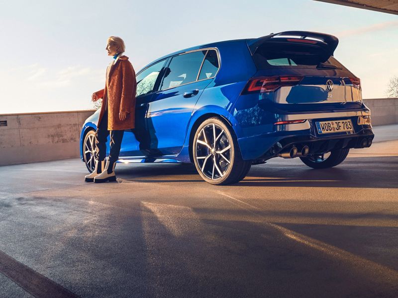 A new Golf R parked in a car park with a lady leaning on the passenger door