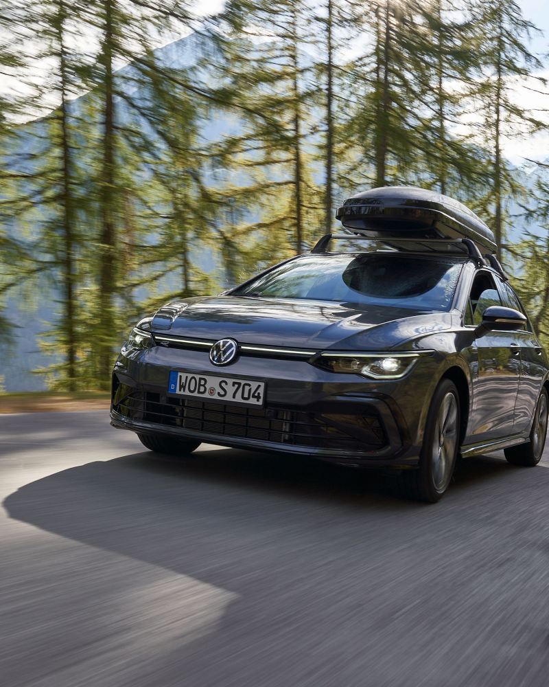 Ένα VW Golf με μπαγκαζιέρα οροφής, ένα δάσος και βουνά στο φόντο