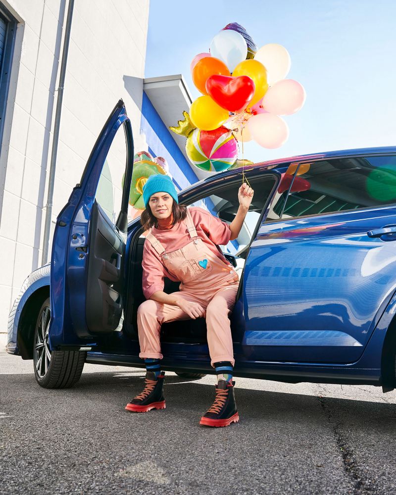 Una mujer con globos de colores en sus manos está sentada en un coche VW abierto