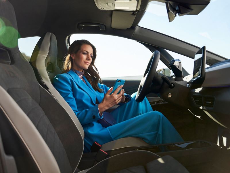 Een vrouw zit in een VW ID.3 en kijkt op haar mobiele telefoon – hulp bij apps en digitale diensten