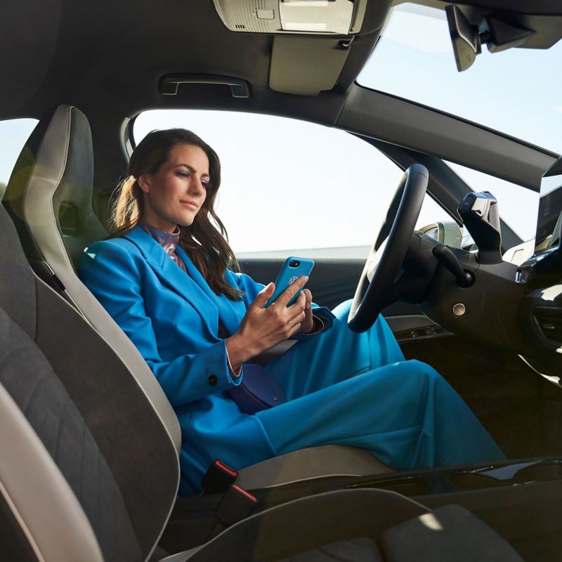 Een vrouw zit in een VW ID.3 en kijkt op haar mobiele telefoon – hulp bij apps en digitale diensten
