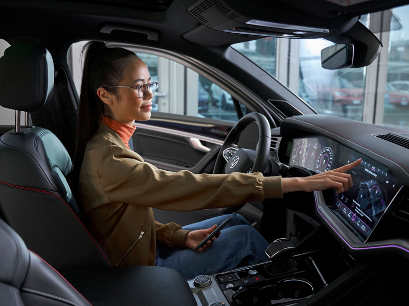 Eine Frau sitzt im VW ID. Auto und bedient Infotainment-System – Hilfe zu Apps und digitalen Diensten