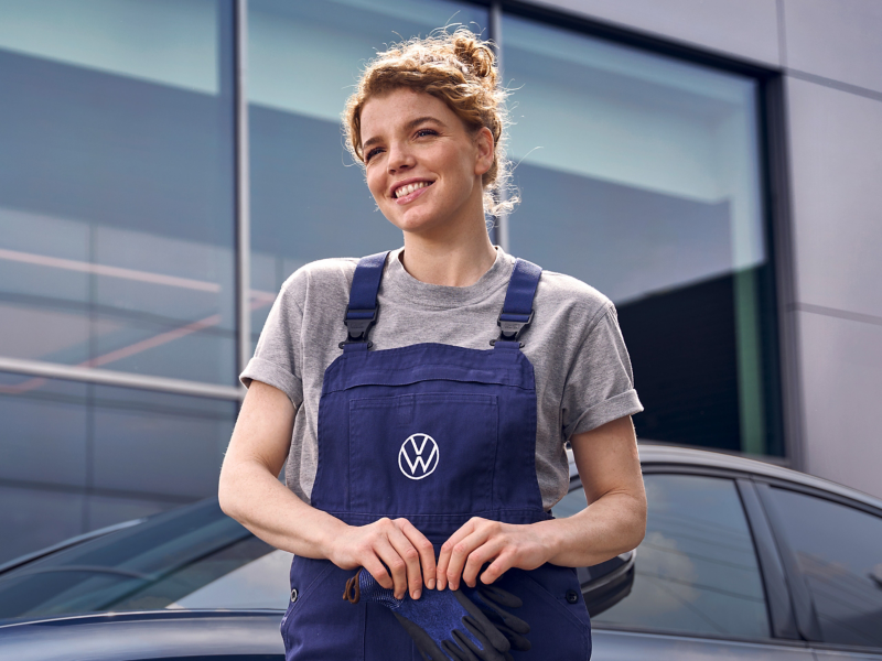 VW Servicemitarbeiterin lächelnd vor Volkswagen Werkstatt