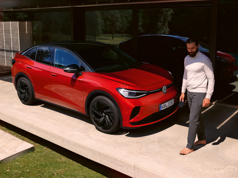 Un véhicule VW ID5. GTX rouge sous un carport moderne, un homme longe le capot avant