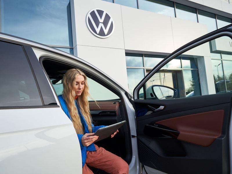 A woman sits inside her VW ID. in front of a workshop and holds a tablet in her hands