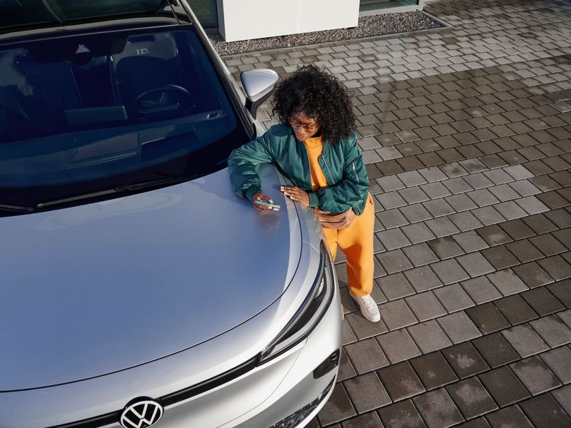 Una chica con un móvil apoyada en el capó de un modelo Volkswagen ID.