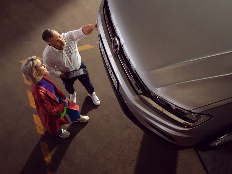 Eine Kundin und ein VW Servicemitarbeiter sprechen über ihr Auto – Inspektion und Reparatur