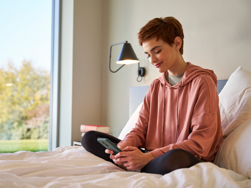 Frau sitzt auf Bett und schaut auf Smartphone – Digitale Live Beratung zu ID. Modellen