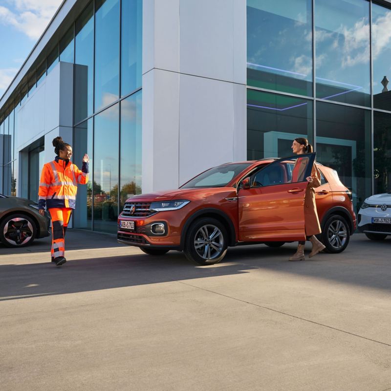 VW Servicemitarbeiterin grüßt Kundin, die in ein VW Auto steigt – Mobilitätsgarantie