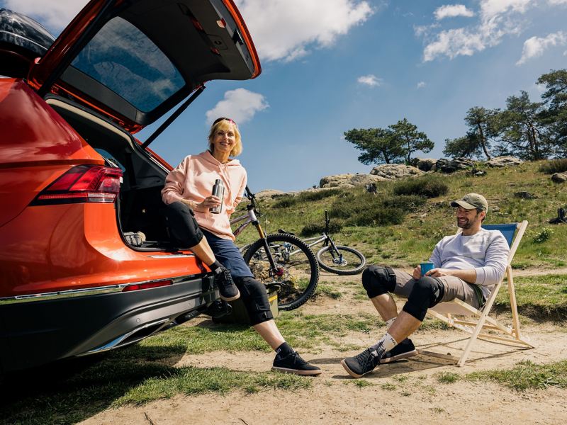 Eine Frau lehnt an ihrem VW und ein Mann sitzt auf einem Klappstuhl – modellspezifisches Zubehör