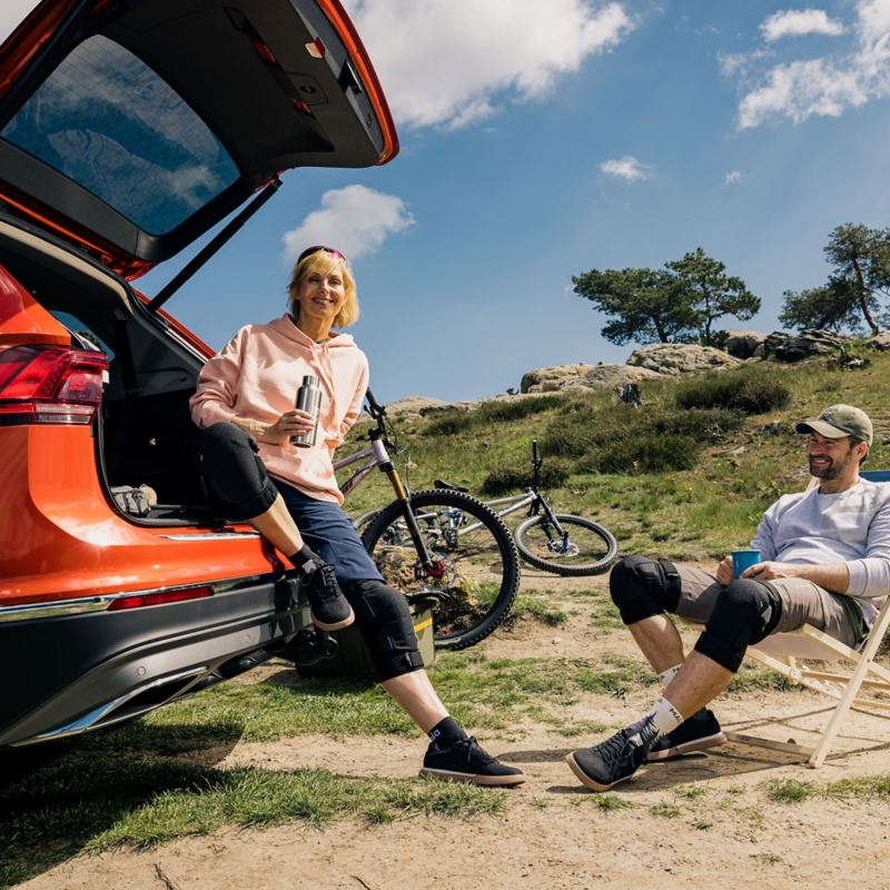 Eine Frau lehnt an ihrem VW und ein Mann sitzt auf einem Klappstuhl – modellspezifisches Zubehör