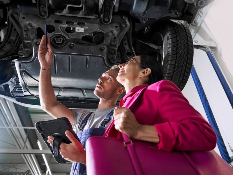 VW Servicemitarbeiter und Kundin schauen sich gemeinsam den Unterboden eines VW Autos an