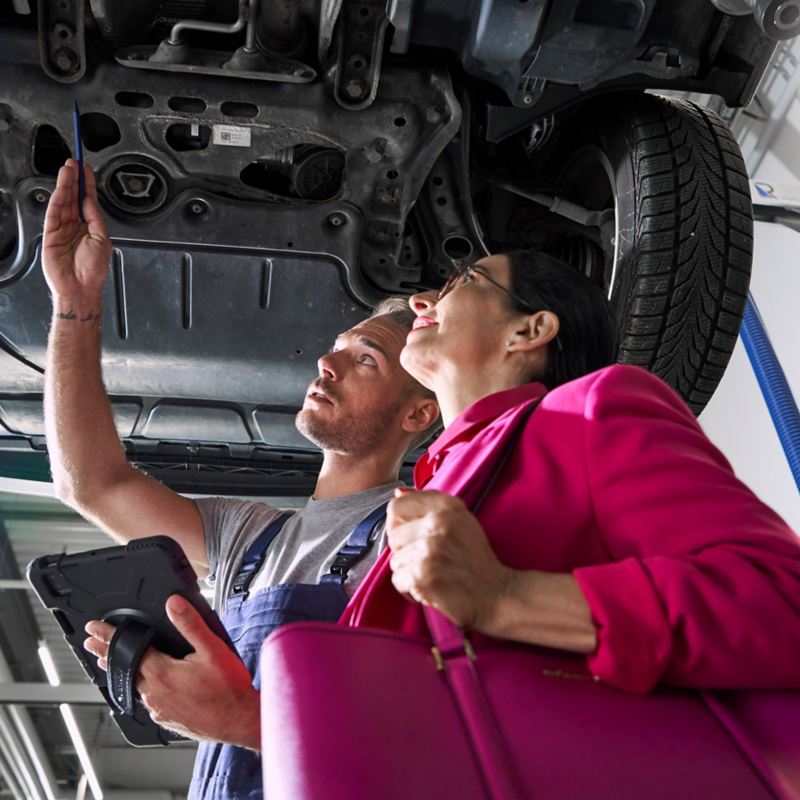 VW Servicemitarbeiter und Kundin schauen sich gemeinsam den Unterboden eines VW Autos an