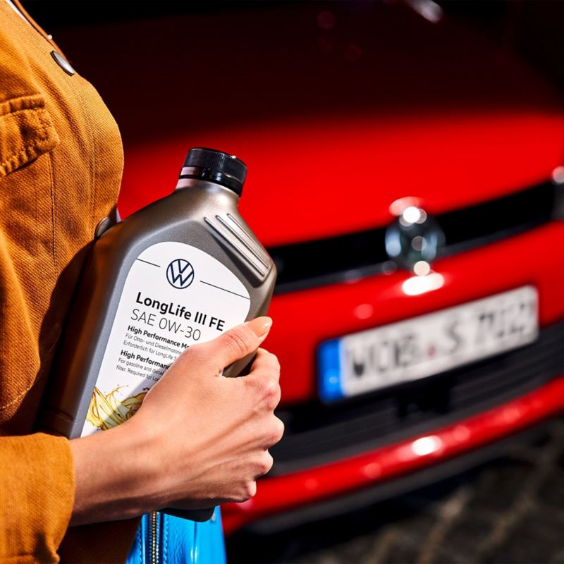 Eine Frau steht vor einem Volkswagen und hält eine Motorenölflasche in der Hand
