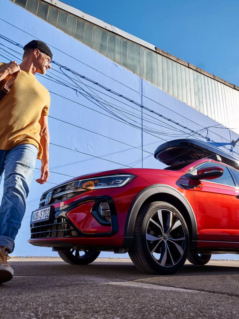 Un homme marche devant sa Volkswagen rouge avec un coffre de toit
