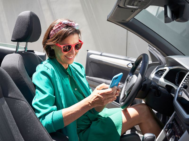 Eine Frau mit Smartphone in der Hand sitzt in einem VW Auto