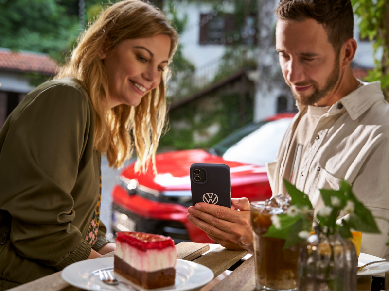 Pärchen sitzt in einem Café und liest VW Newsletter auf Smartphone