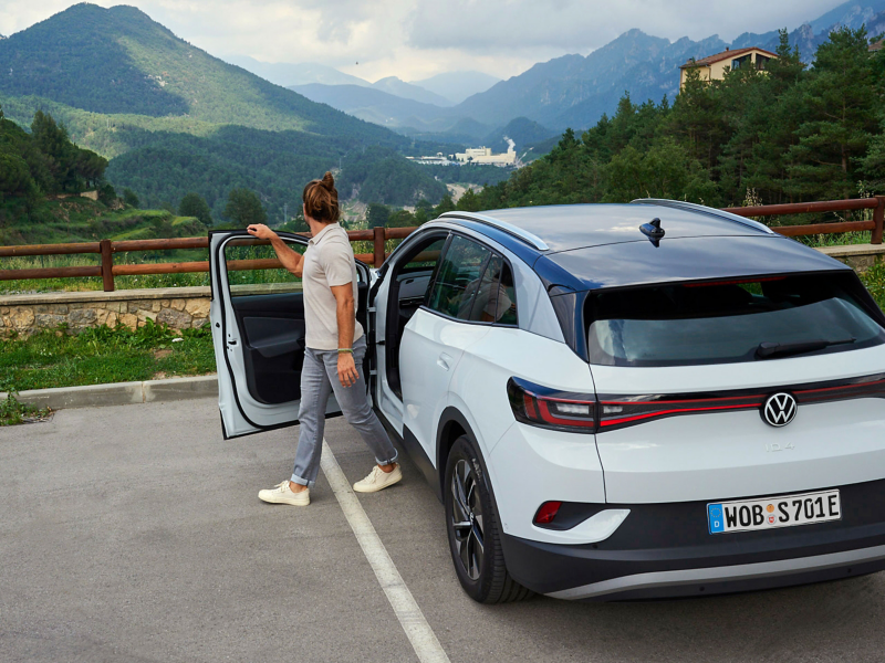 Ein Mann steigt aus seinem weißen VW Elektroauto aus und schaut auf die Berge