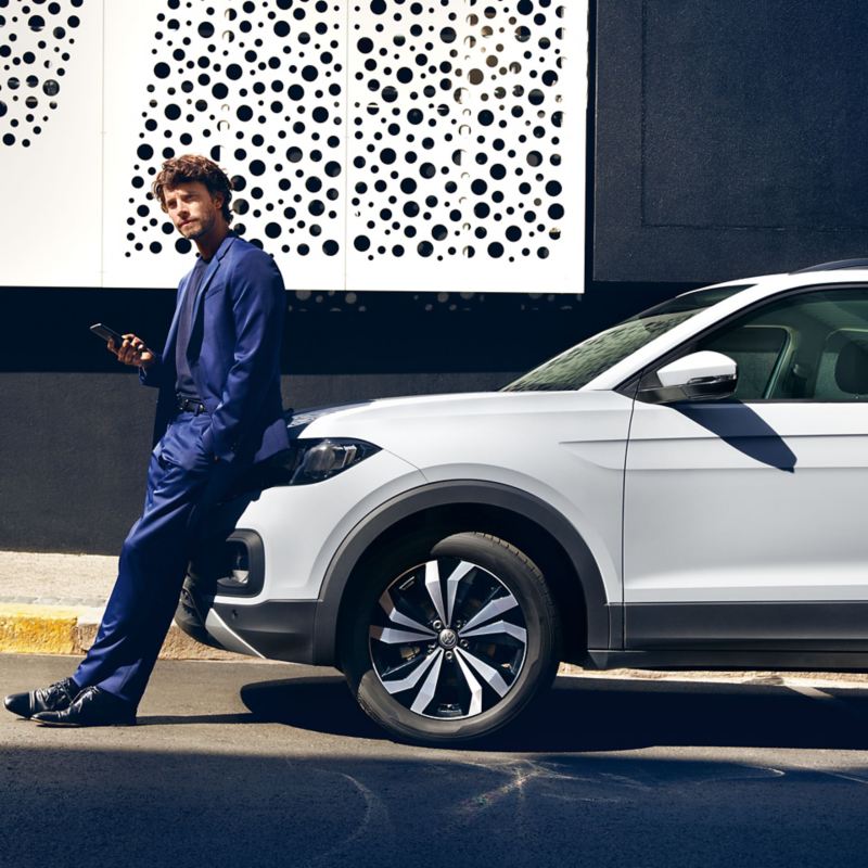 Mann lehnt am Volkswagen und hält sein Smartphone in der Hand