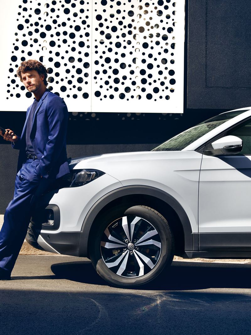 Mann lehnt am Volkswagen und hält sein Smartphone in der Hand