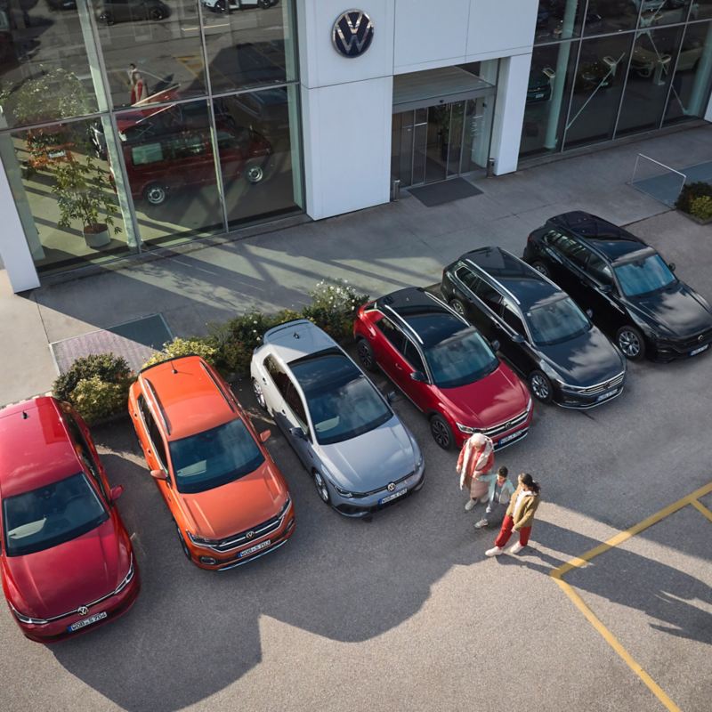 A family next to six Volkswagen previous models in a car park