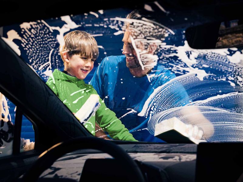 Un uomo e un bambino lavano il parabrezza della loro auto Volkswagen prima di partire per un viaggio.