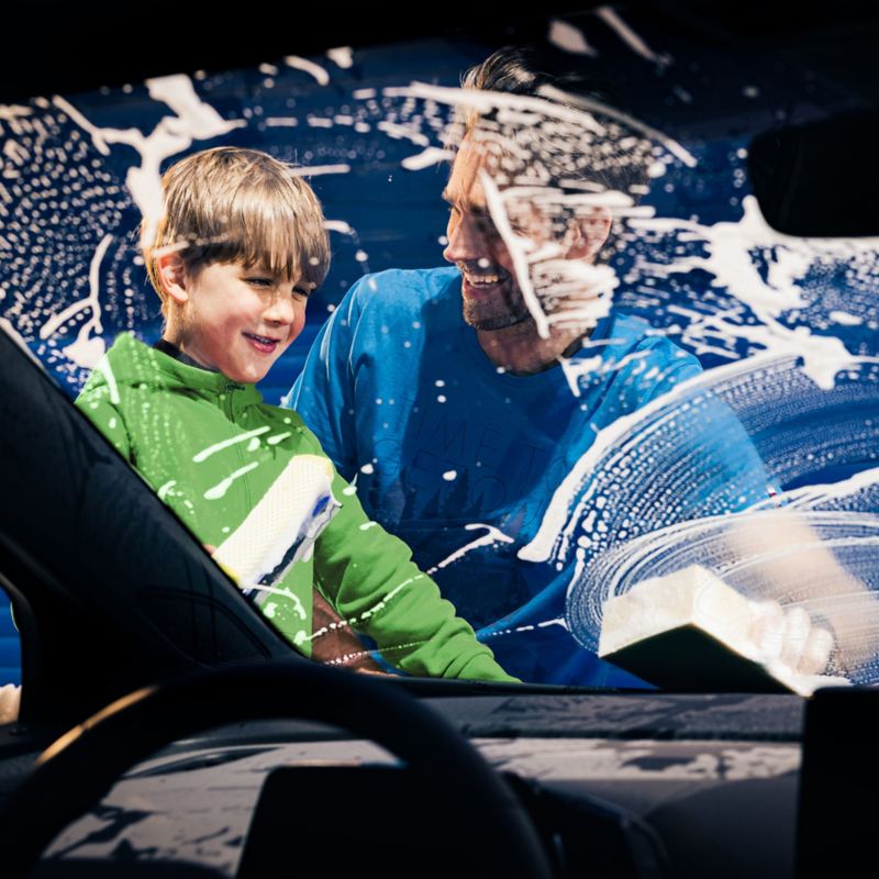  フォルクワーゲン車のフロントガラスをフォルクスワーゲンケア製品で洗う父親と息子