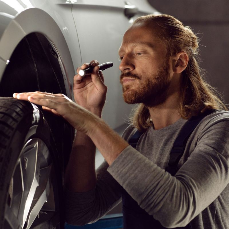 Ein VW Servicemitarbeiter inspiziert die Reifen eines Volkswagen