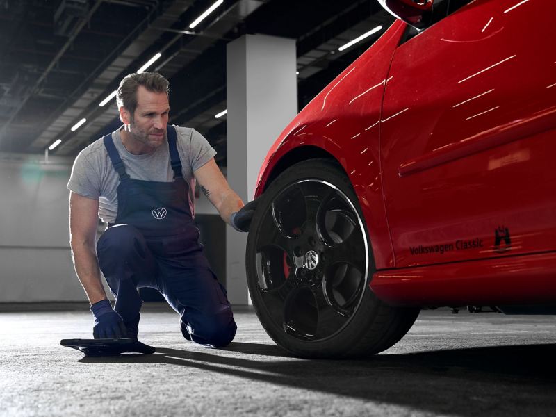 Ein VW Servicemitarbeiter schaut sich den Autoreifen eines roten VW an – Räderwissen