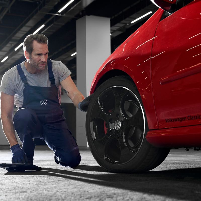 Ein VW Servicemitarbeiter schaut sich den Autoreifen eines roten VW an – Räderwissen