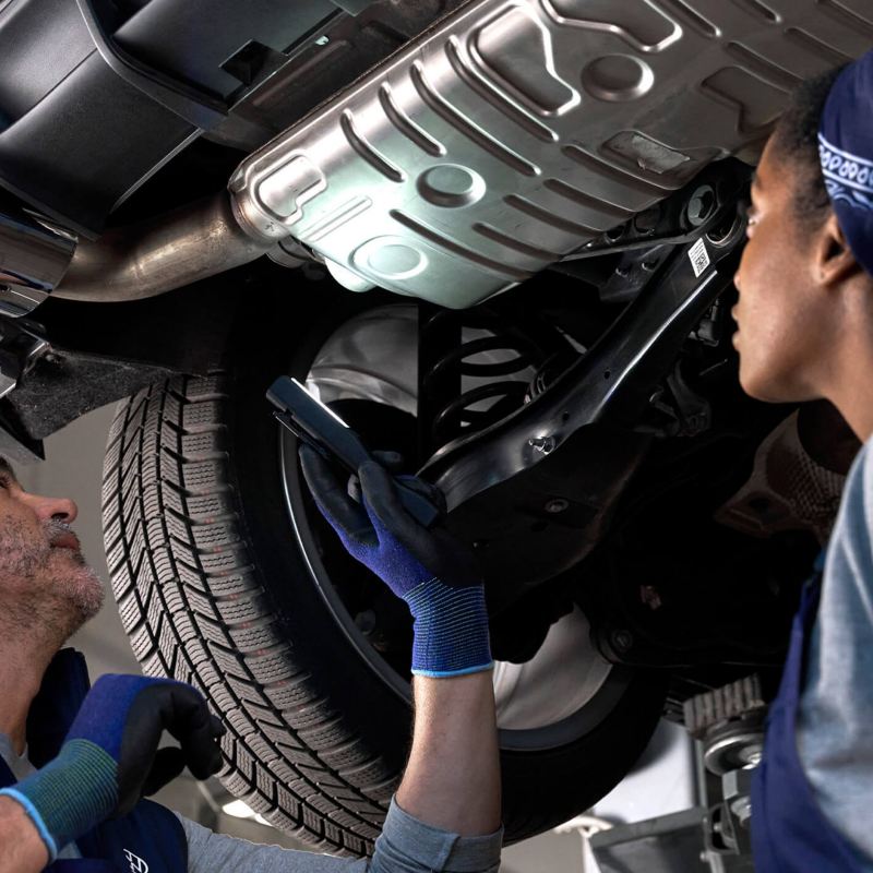 Two VW technicians inspecting the underside of a VW vehicle. 